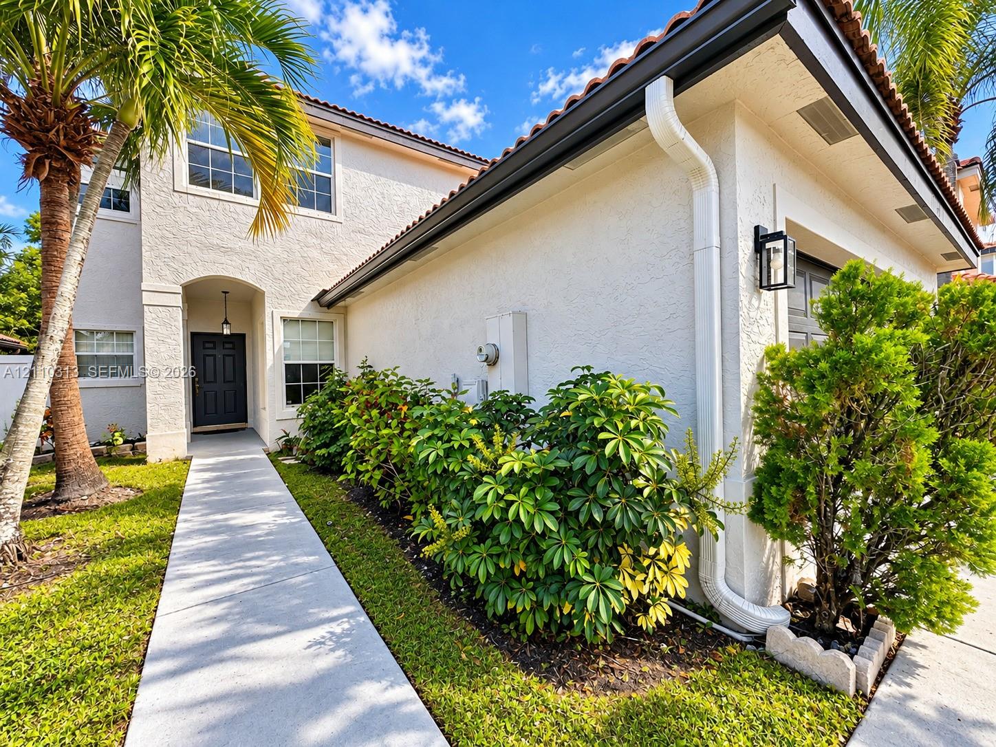 Stucco exterior featuring a concrete walkway, multi-pane windows, terra cotta roof tiles, and an arched entryway