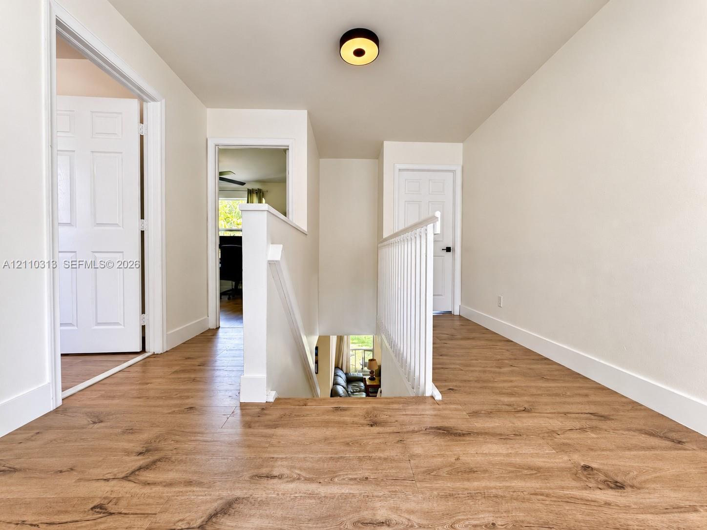Landing area featuring wood-finish flooring, white paneled interior doors, a white wooden staircase railing, and a circular flush-mount ceiling light fixture