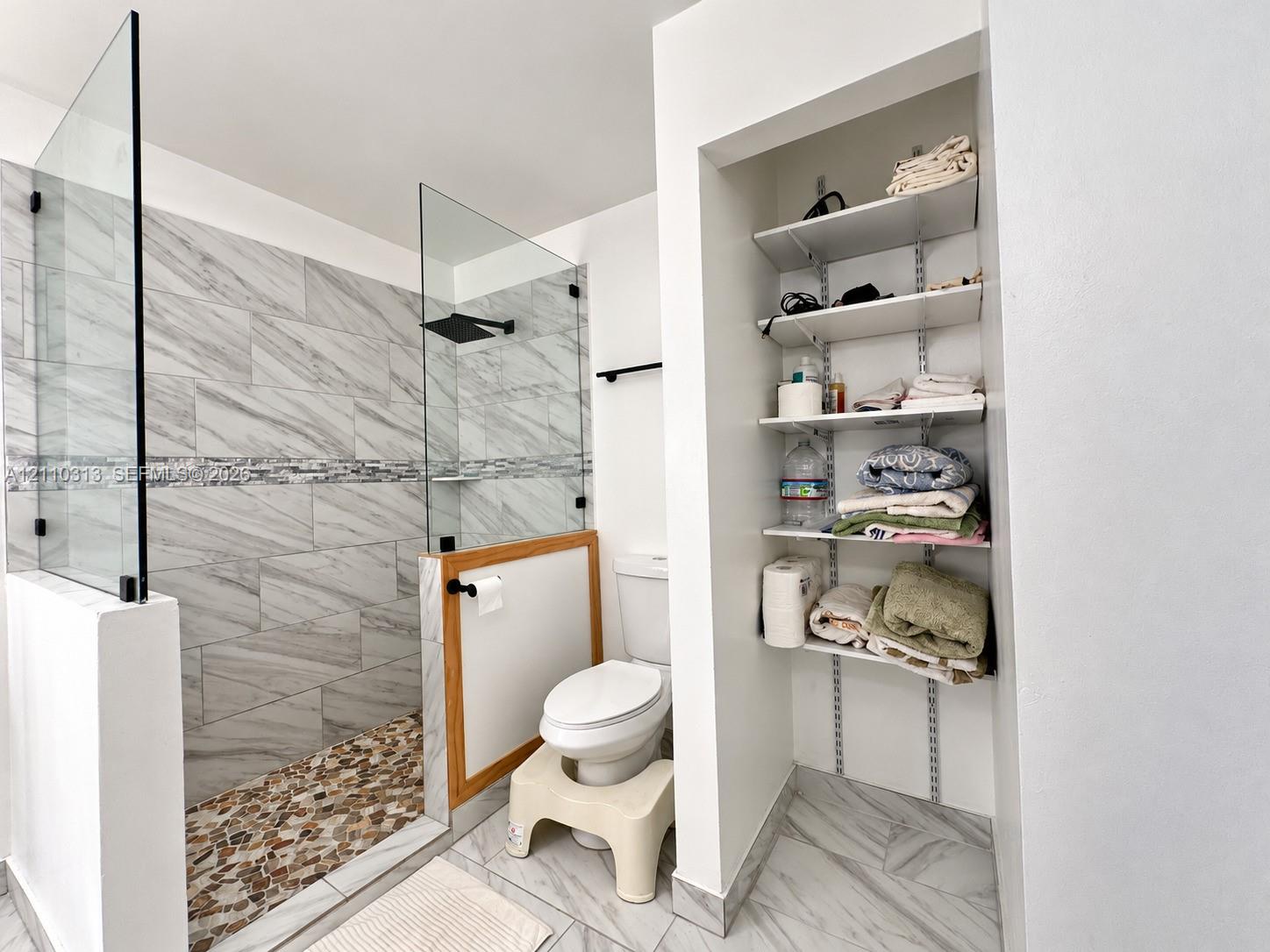 Walk-in shower featuring a glass enclosure, rainfall showerhead, and multi-tone pebble flooring