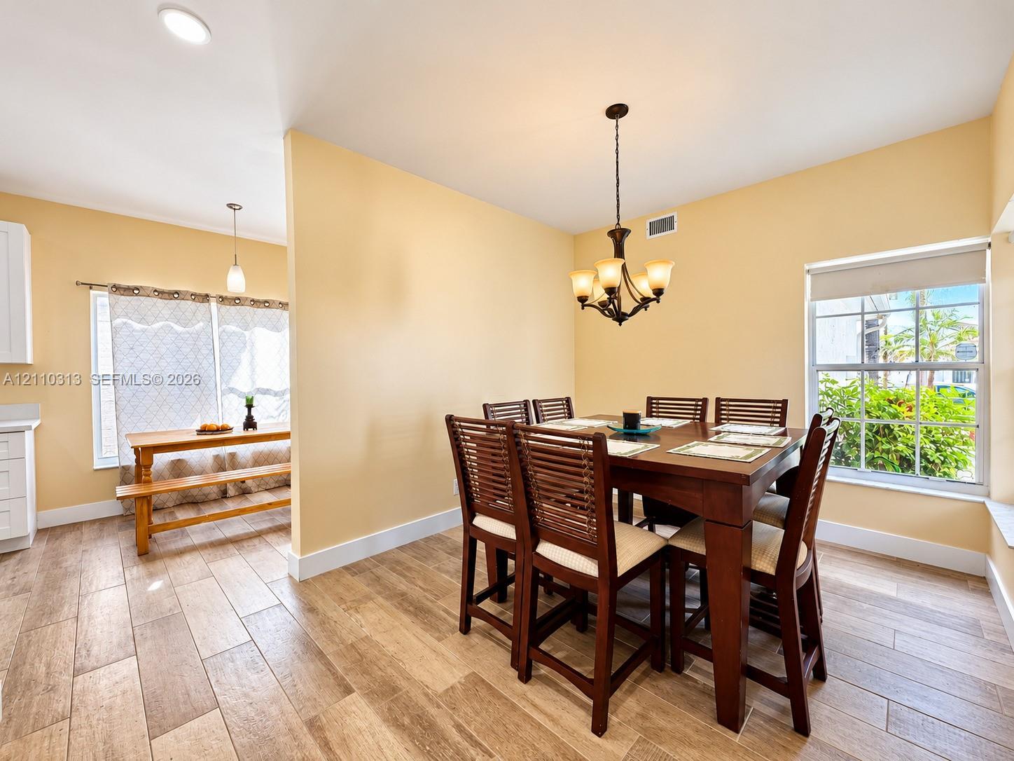 Wood-finish tile flooring, multi-light chandelier, recessed lighting, and large windows providing natural illumination