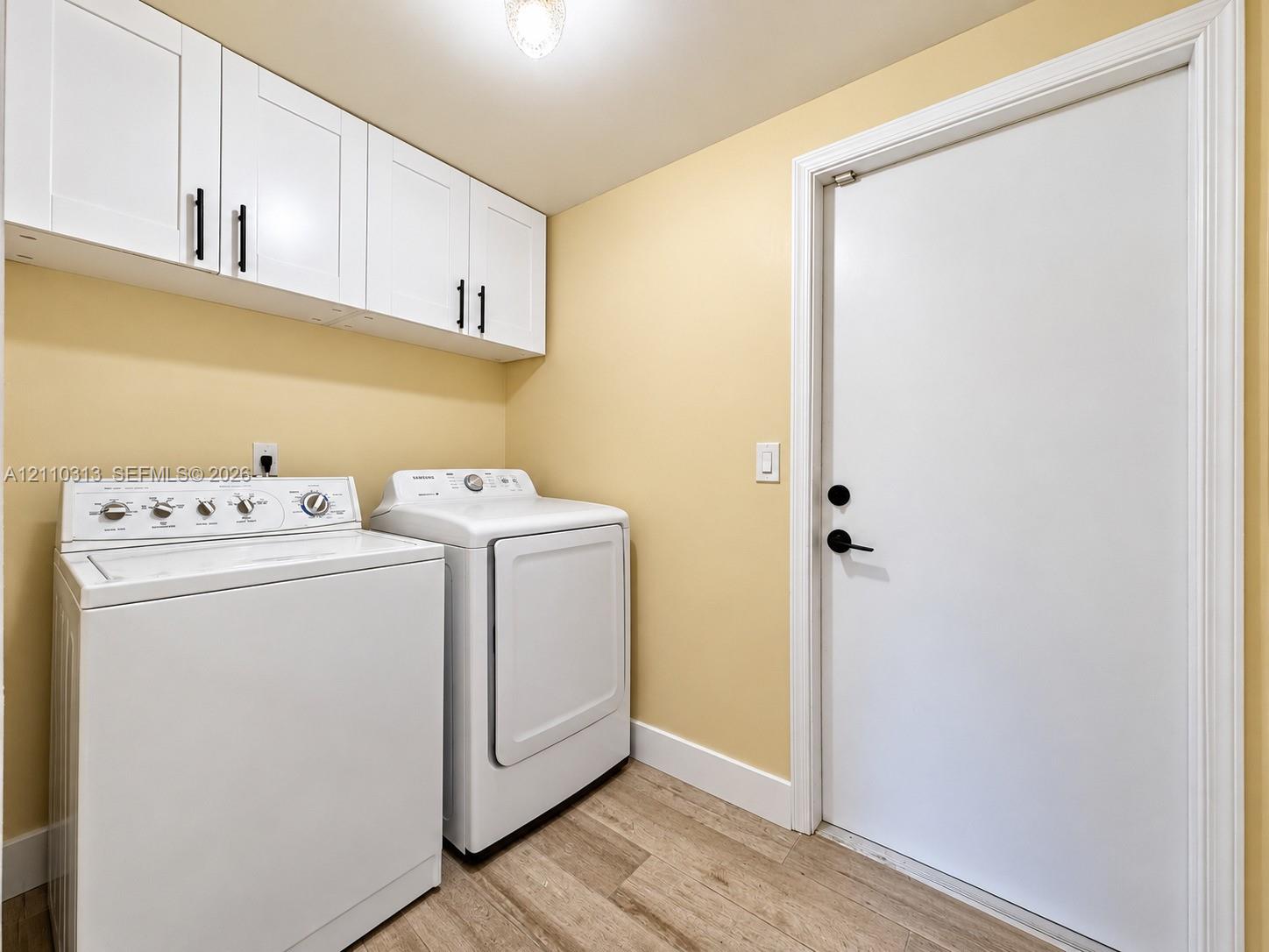 Shaker-style white cabinetry with matte black hardware, wood-finish flooring, and a solid-panel door with matte black lever handle