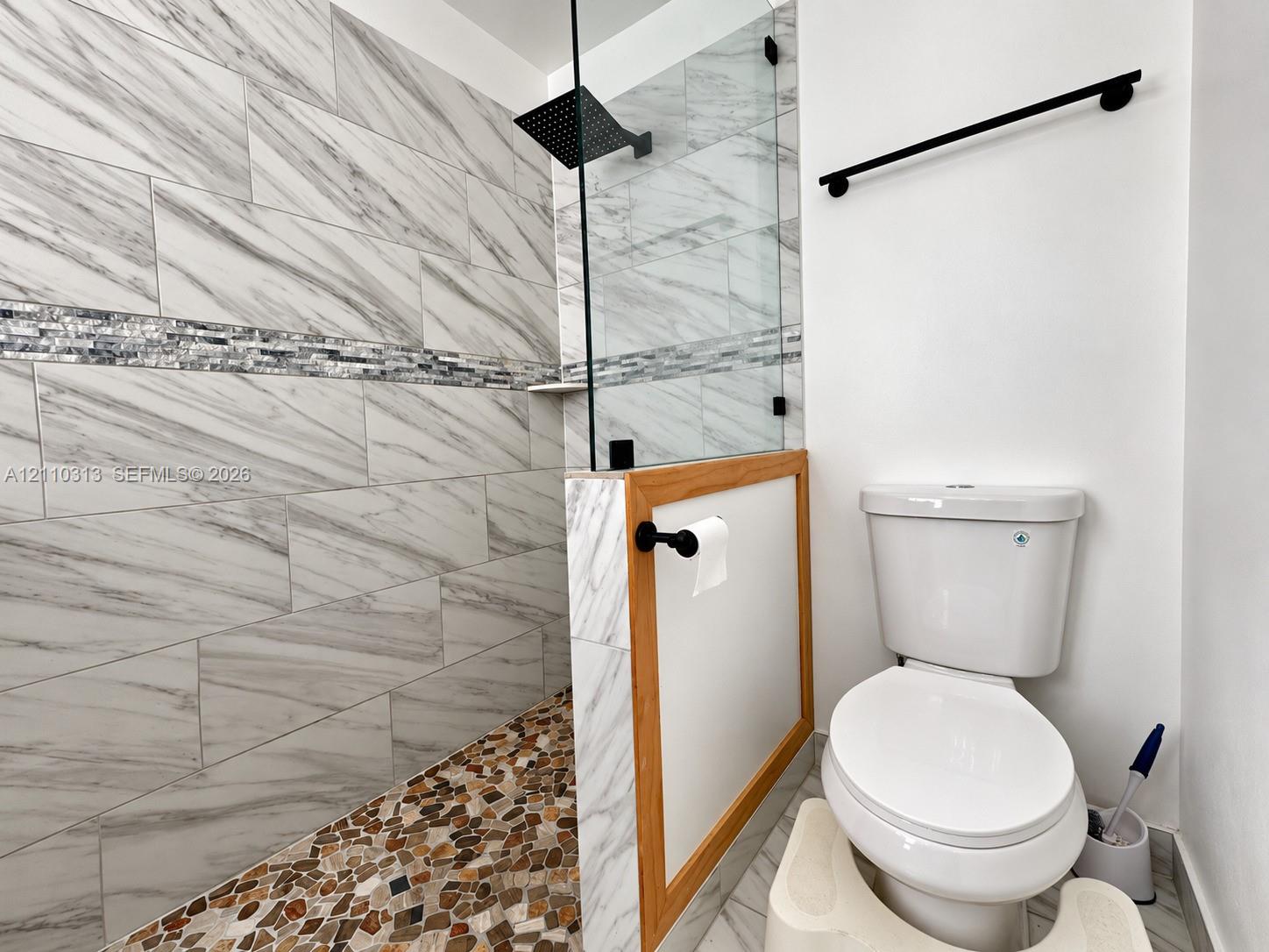 Walk-in shower with stone-tiled flooring, large-format wall tile, glass enclosure, and a square matte black shower head