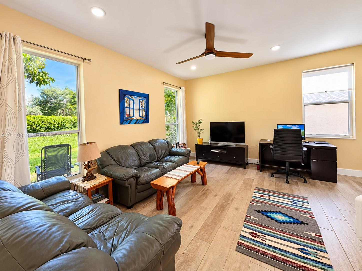 Wood-finish tile flooring, recessed ceiling lighting, three large picture windows, and a ceiling fan