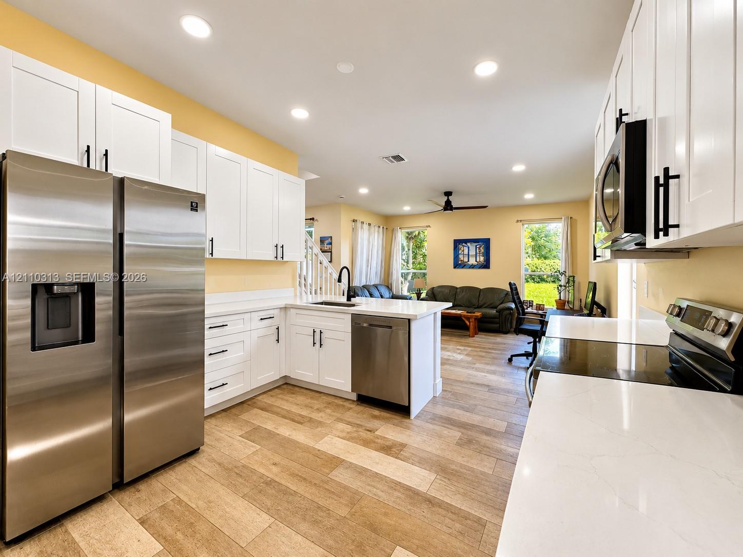 Kitchen featuring white cabinetry with dark hardware, stone-finish countertops, stainless steel appliances, and wood-finish flooring