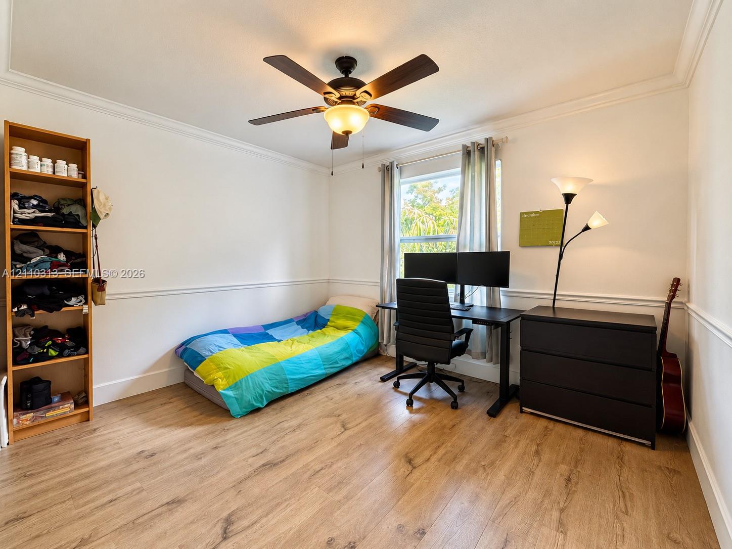 Room featuring wood-finish flooring, chair rail molding, crown molding, and a central ceiling fan with an integrated light fixture