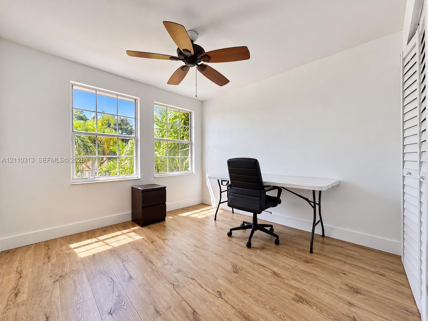 Wood-finish flooring, dual grid-pattern windows, ceiling fan with wood-tone blades, and louvered bi-fold closet doors