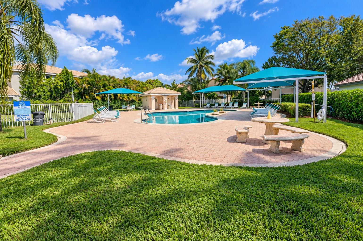Community pool featuring a paved deck, permanent shaded structures, built-in masonry seating, and manicured landscaping