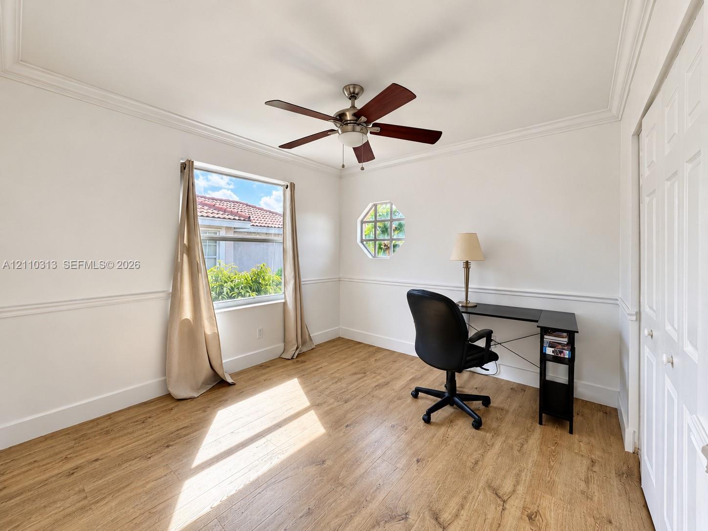 Room featuring wood-finish flooring, crown molding, chair rail trim, an octagonal window, and a ceiling fan with integrated light fixture