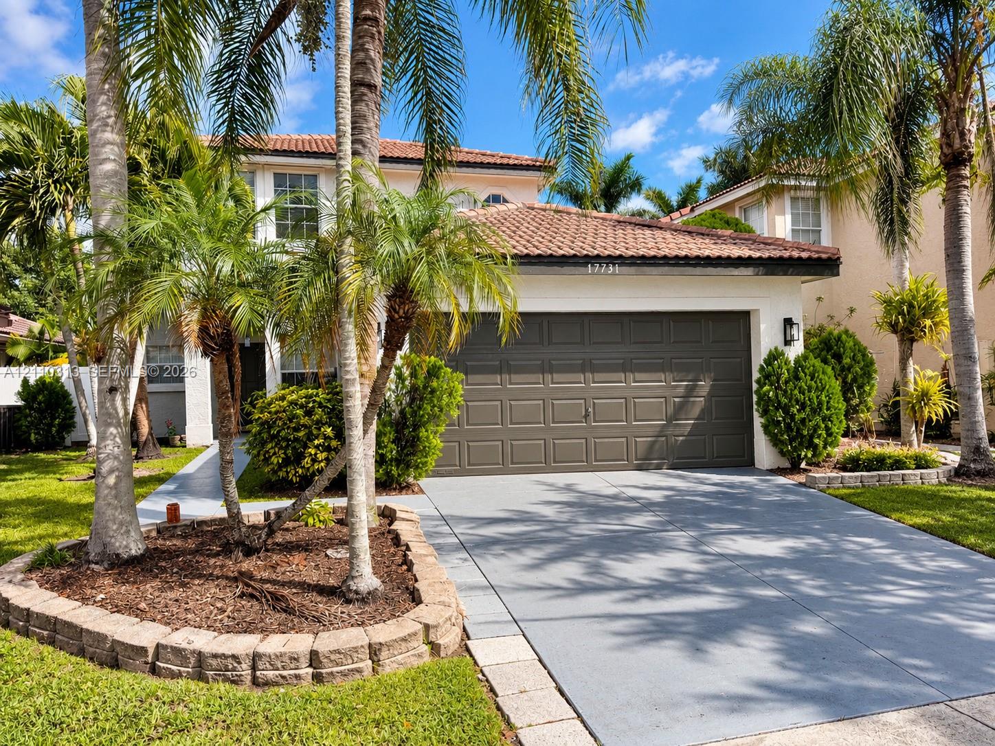 Stucco exterior featuring a clay tile roof, two-car garage, concrete driveway, and stone-bordered landscaping beds