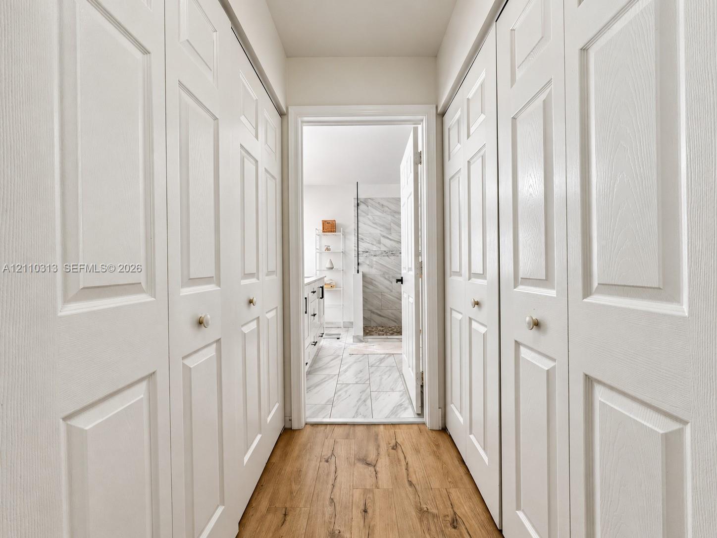 Hallway featuring four white multi-panel bi-fold doors, wood-finish flooring, and stone-tile flooring in the interior space