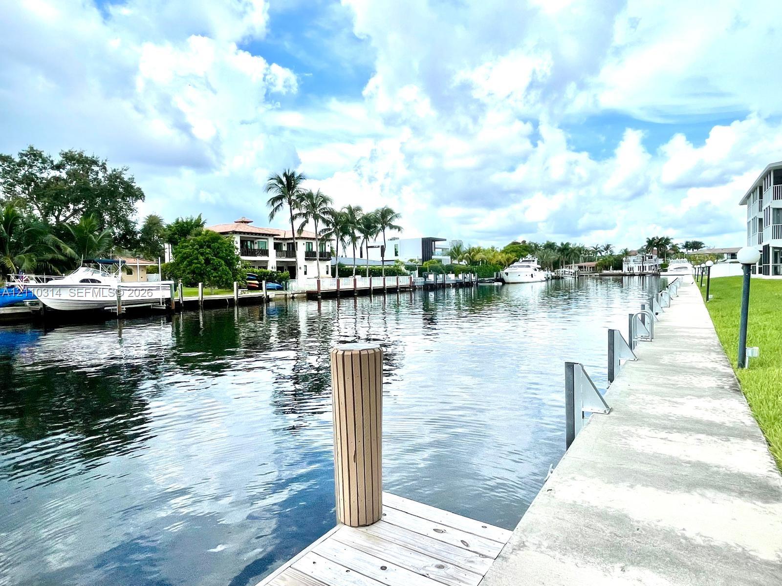 Waterfront property featuring a concrete seawall, wooden dock, mooring pilings, and manicured lawn