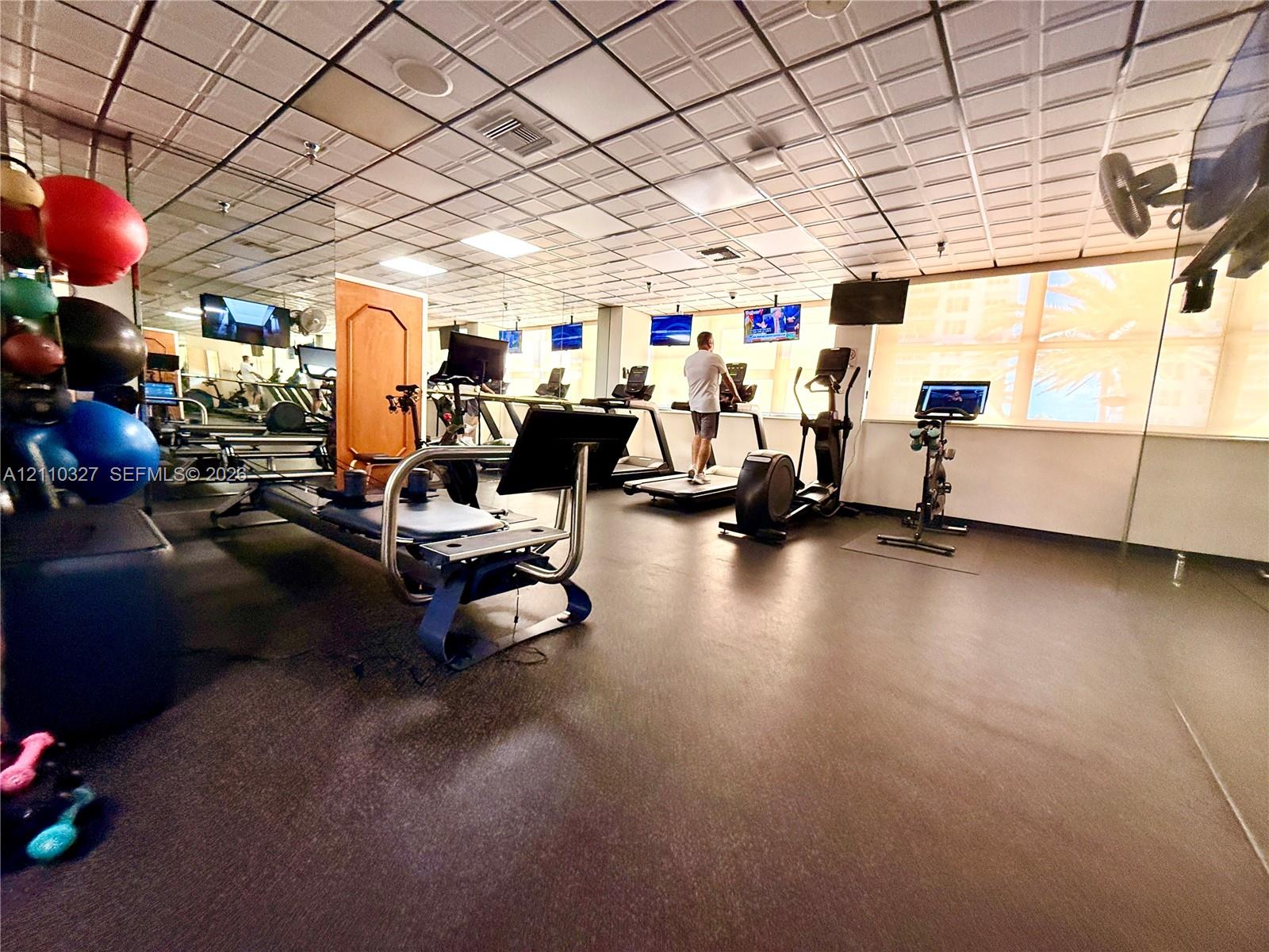 Fitness area featuring a coffered drop ceiling, expansive wall-to-wall mirrors, and durable rubberized flooring