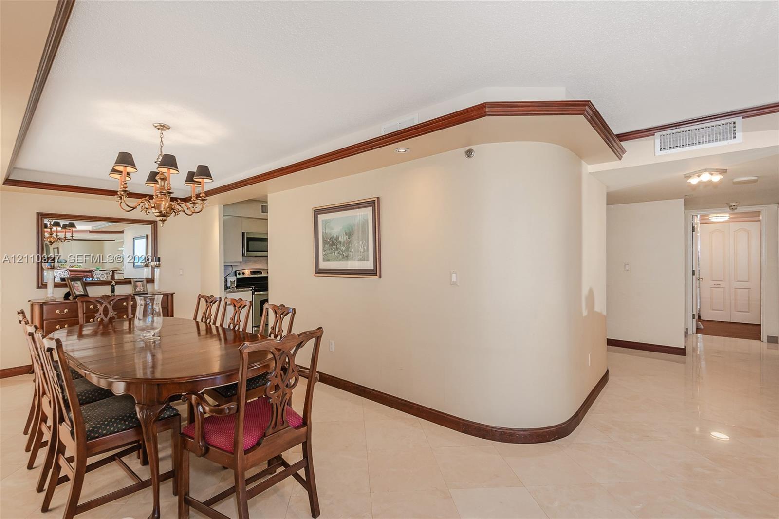 Dining area featuring an ornate multi-arm chandelier, built-in wet bar with mirrored backsplash, and floor-to-ceiling sliding glass doors opening to a tiled balcony with ocean backdrop
