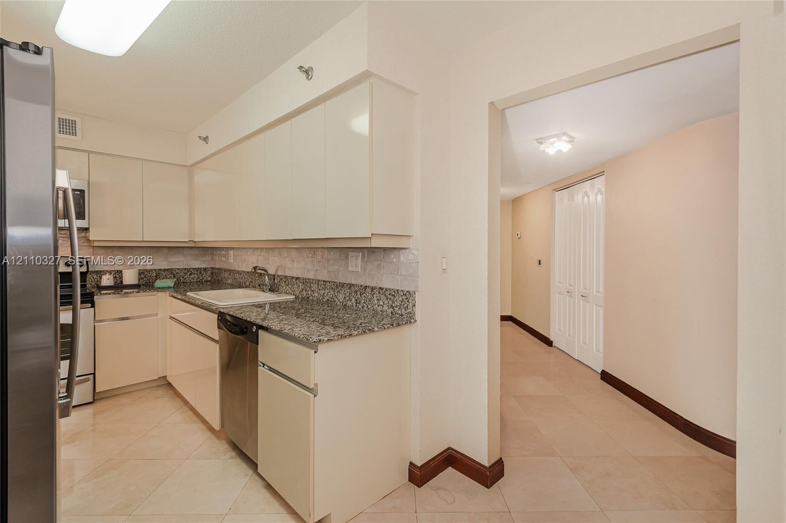 Kitchen featuring flat-panel cabinetry, light-toned stone countertops, a dark-finish double-door refrigerator, and polished stone tile flooring throughout