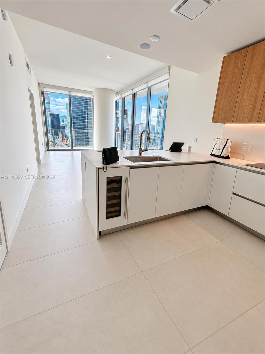 Kitchen featuring custom cabinetry with white lower and wood-finish upper units, integrated wine refrigerator, quartz-surface countertops, and expansive floor-to-ceiling windows