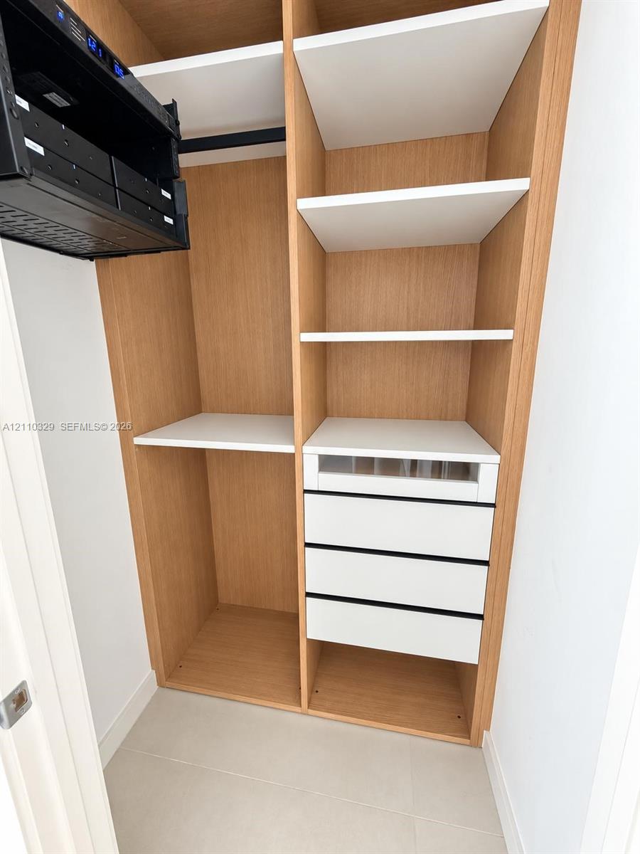 Custom closet featuring wood-finish cabinetry, white shelving, four integrated drawers, and a built-in electronics rack
