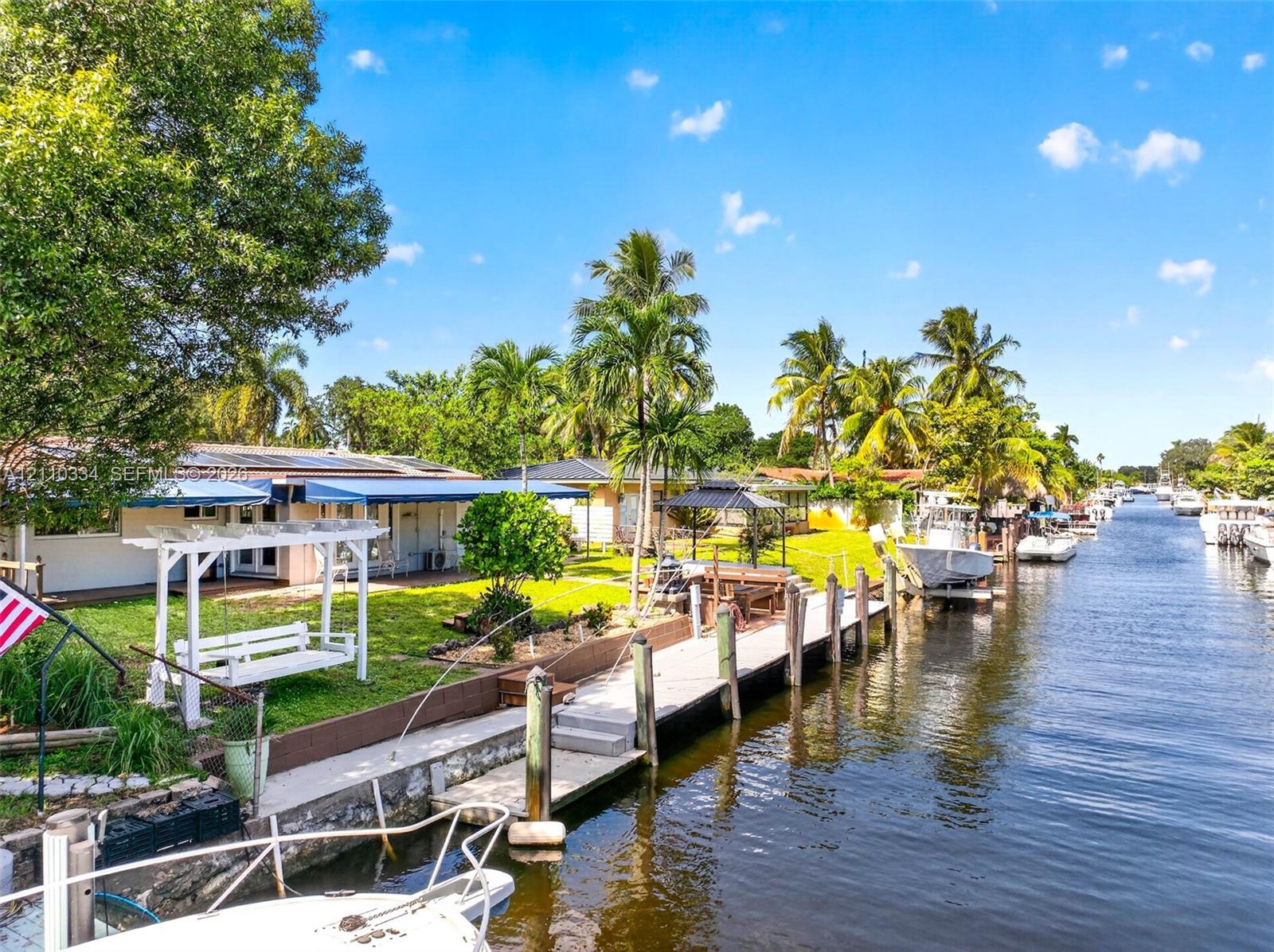 Waterfront property featuring a private concrete boat dock, seawall, landscaped lawn, and retractable exterior awnings