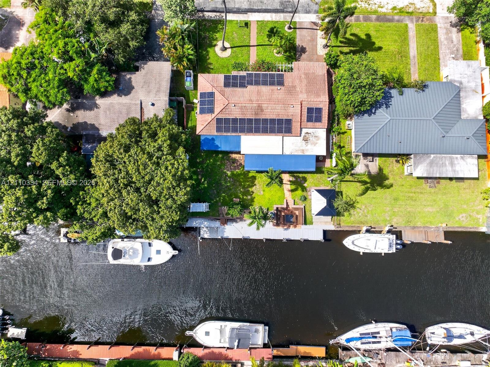 Waterfront property featuring a private dock, solar panel array, tiled roof, mature landscaping, and bulkhead retaining wall