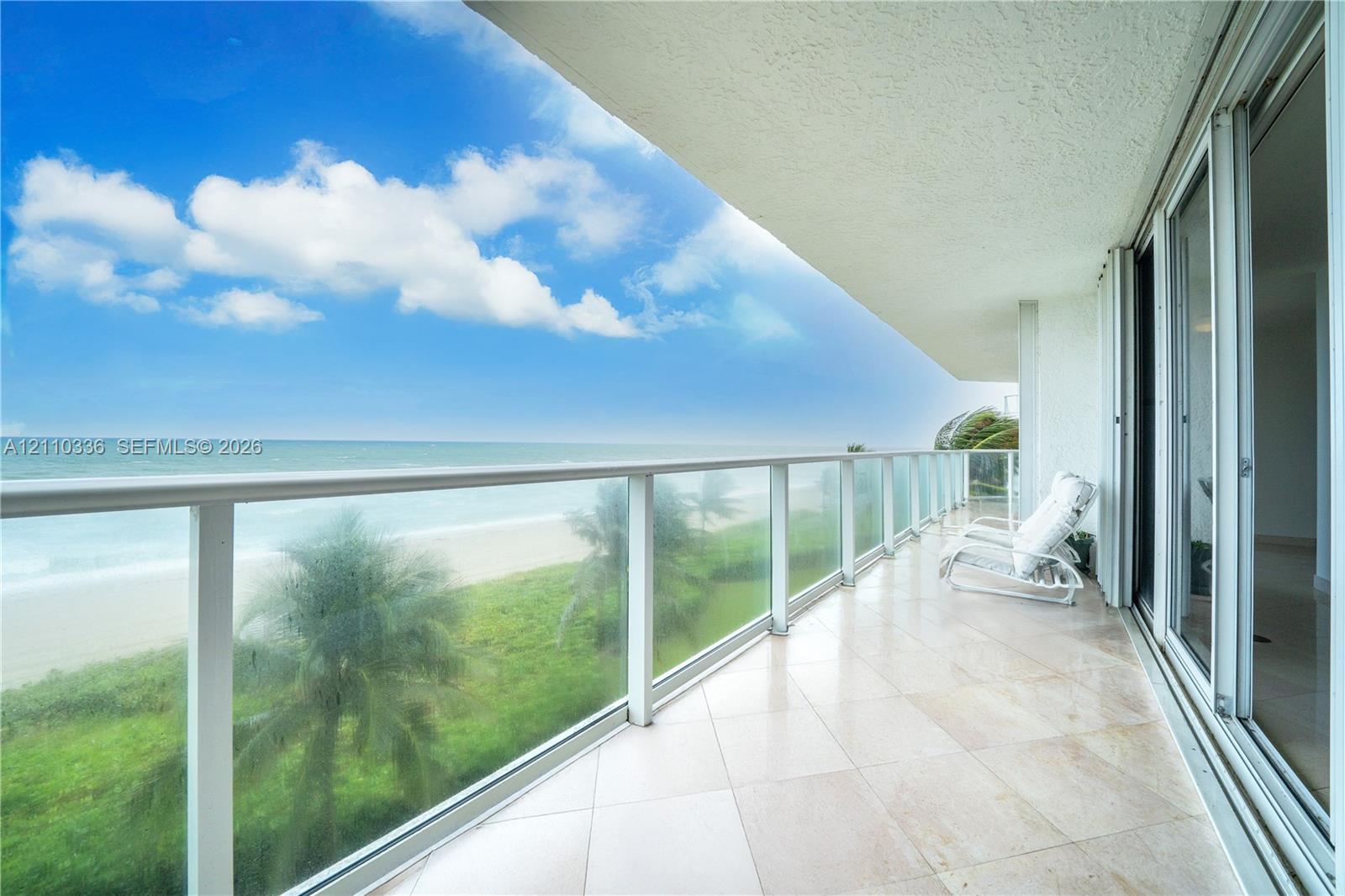 Covered balcony featuring stone tile flooring and a glass railing, encompassing water scenery Covered balcony featuring stone tile flooring and a glass railing, encompassing water scenery