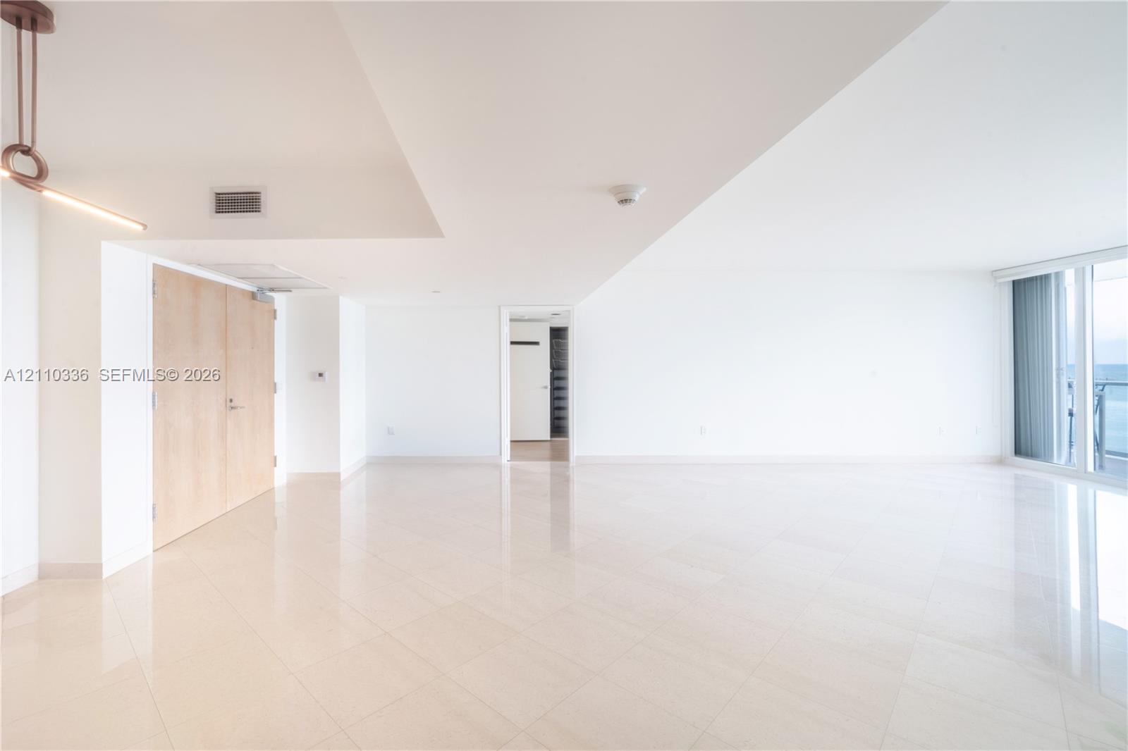 Open-concept interior featuring light-toned tile flooring, floor-to-ceiling windows, natural finish wood doors, and a contemporary linear pendant light fixture