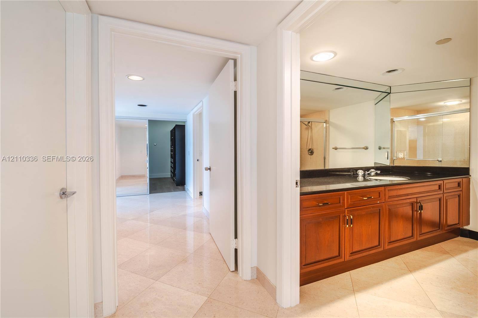 Bathroom featuring a wood-tone vanity, dark solid-surface countertop, full-width mirror, recessed lighting, and stone-finish flooring