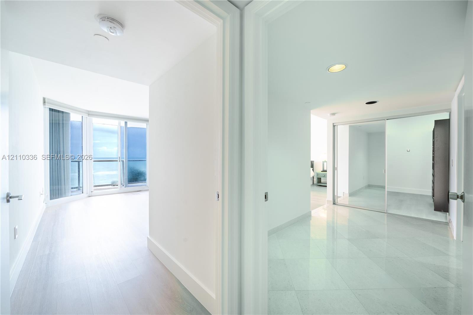 Floor-to-ceiling glass sliding doors, private balcony, large-format tile flooring, and mirrored sliding closet doors