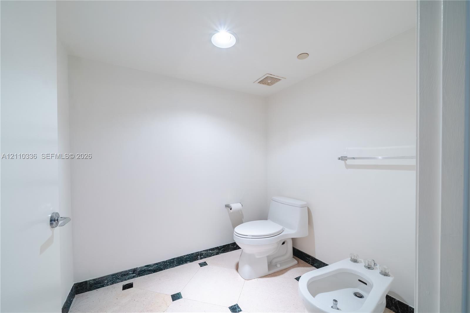 Restroom featuring a dual-piece toilet, porcelain bidet, stone-finish tile flooring with inlaid accents, and a coordinating stone baseboard