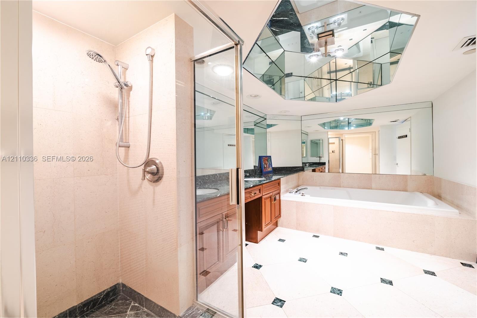 Enclosed shower with handheld fixture, built-in soaking tub, wood-finish cabinetry, stone countertop, and geometric mirrored ceiling accent