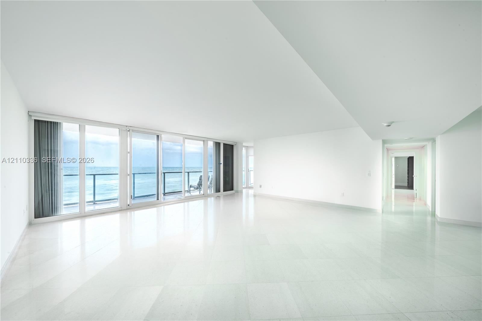 Open-concept interior featuring polished stone flooring, floor-to-ceiling glass sliding doors, and a private balcony with metal railing Open-concept interior featuring polished stone flooring, floor-to-ceiling glass sliding doors, and a private balcony with metal railing