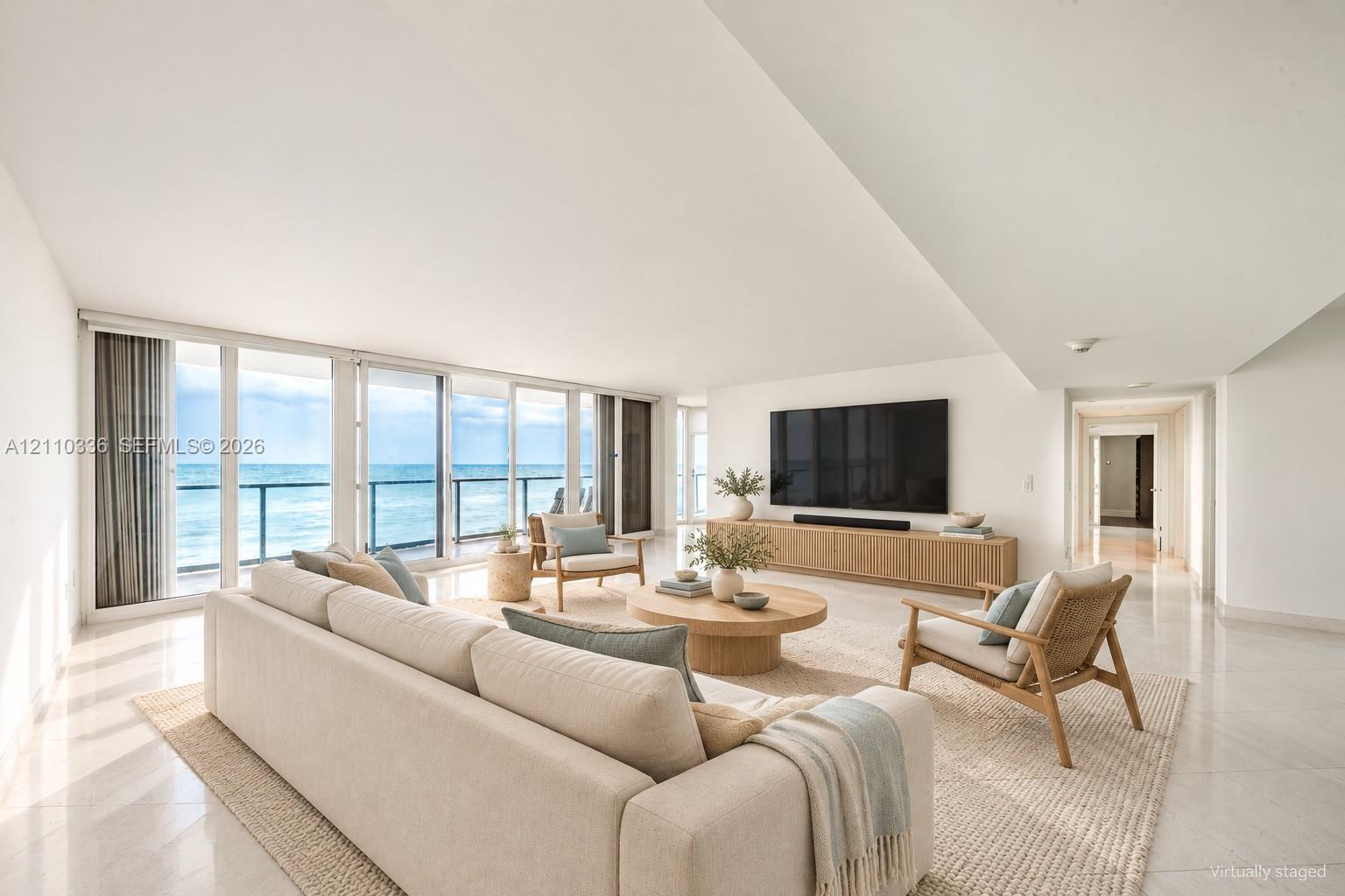 Expansive living space featuring floor-to-ceiling glass panel doors, a balcony with a metal railing, polished stone flooring, and a built-in wood-finish media console