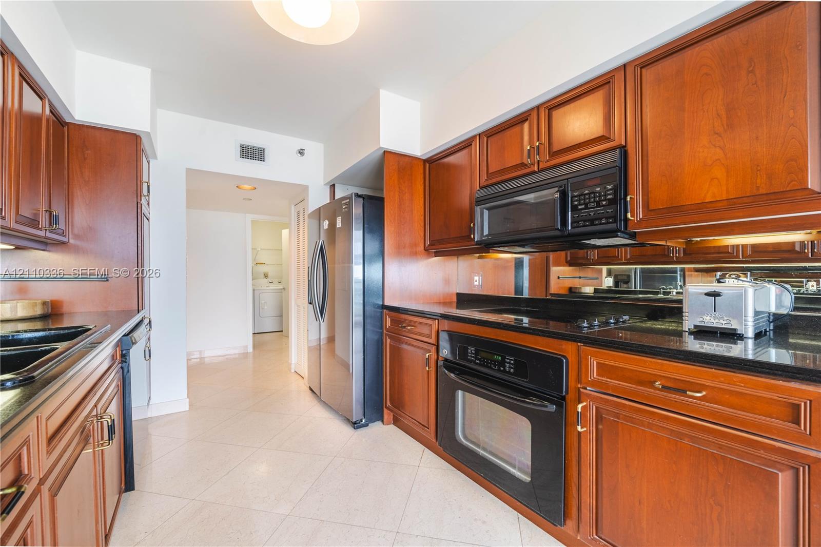 Kitchen featuring warm-toned wood cabinetry, dark stone countertops, mirror backsplash, stainless steel appliances, and tile flooring