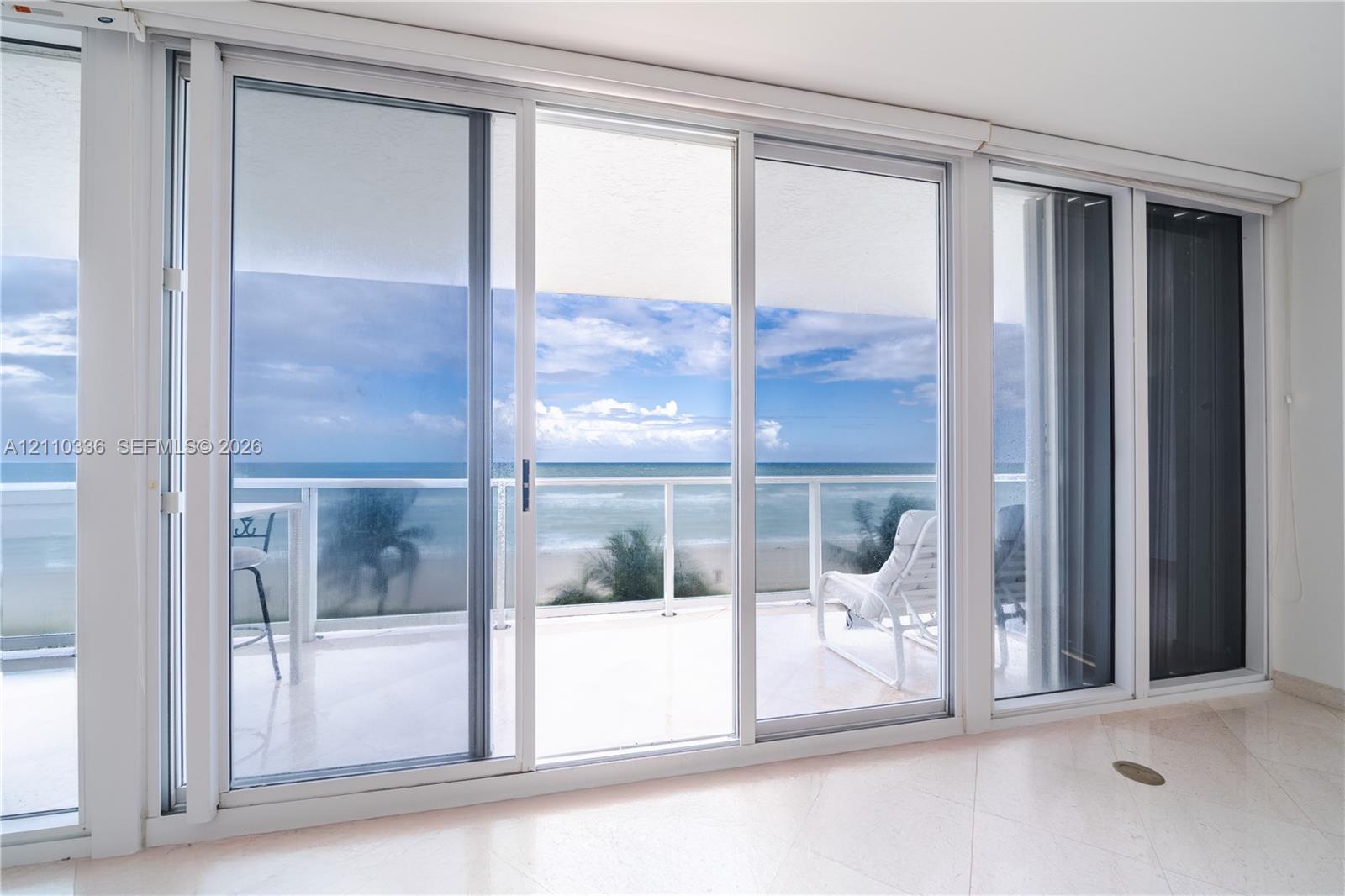 Floor-to-ceiling sliding glass panels, balcony with glass railing, stone flooring, and expansive ocean scenery Floor-to-ceiling sliding glass panels, balcony with glass railing, stone flooring, and expansive ocean scenery