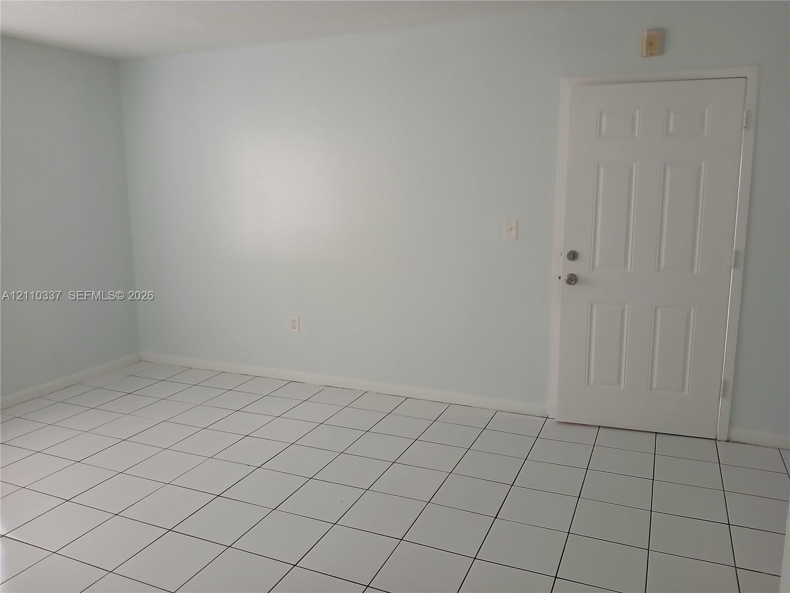 Interior room featuring large-format square tile flooring, neutral wall paint, and a six-panel entry door with metallic hardware