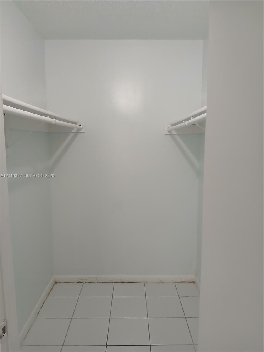 Reach-in storage area featuring white tile flooring and dual-level hanging rods
