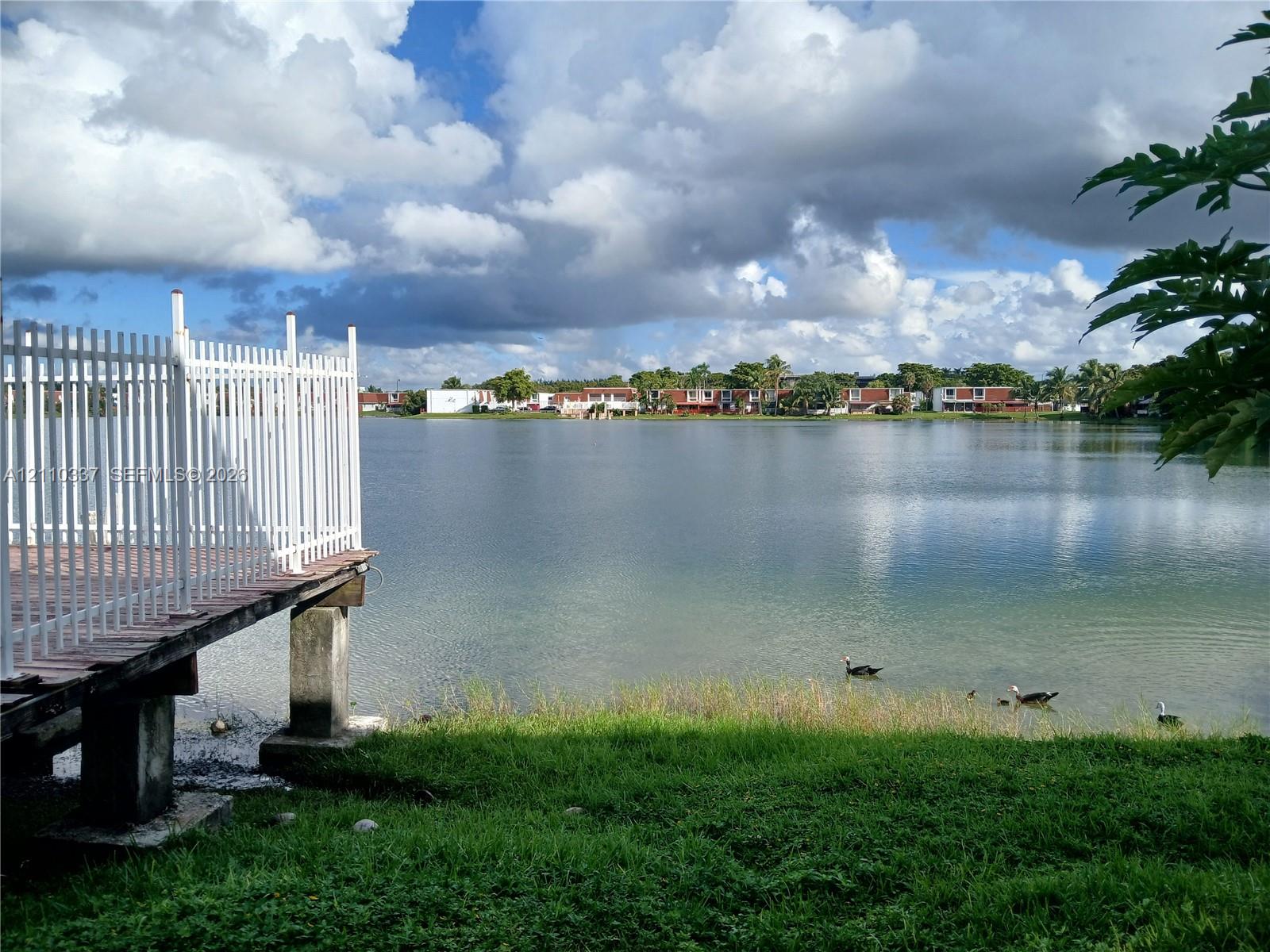 Waterfront parcel featuring a concrete dock, white vertical railing, and maintained lawn bordering the shore
