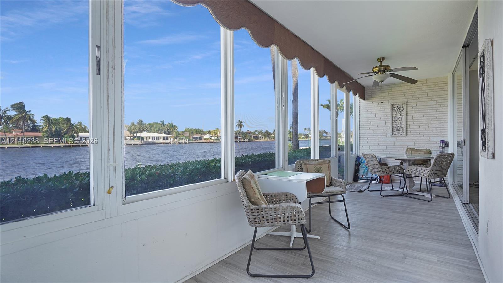 Enclosed lanai featuring full-height glass window walls, painted brick wall finish, wood-finish flooring, and a ceiling fan Enclosed lanai featuring full-height glass window walls, painted brick wall finish, wood-finish flooring, and a ceiling fan