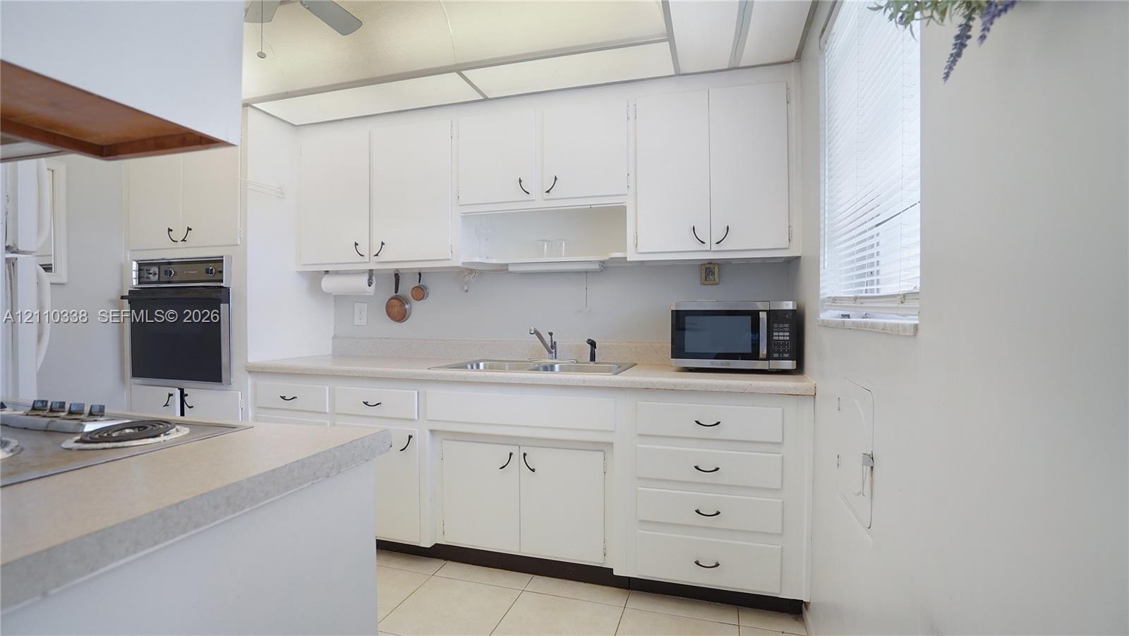 Kitchen featuring white cabinetry, integrated wall oven, laminate countertops, dual-basin sink with retractable faucet, and tile flooring