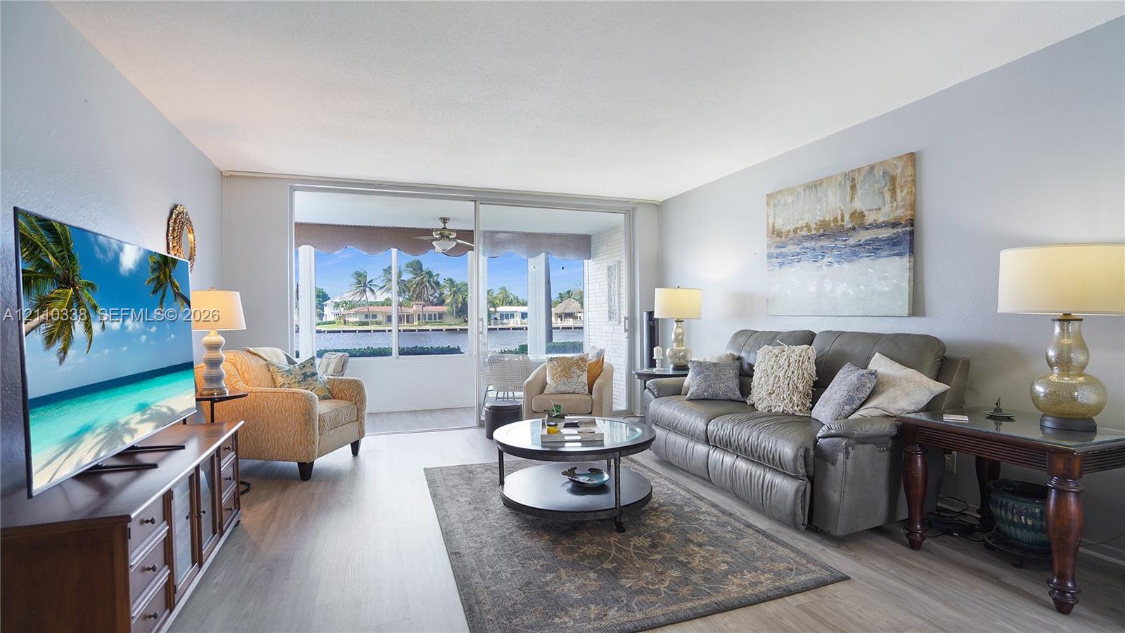 Living area featuring wood-finish flooring, neutral wall paint, and floor-to-ceiling sliding glass doors opening to a screened lanai with water backdrop
