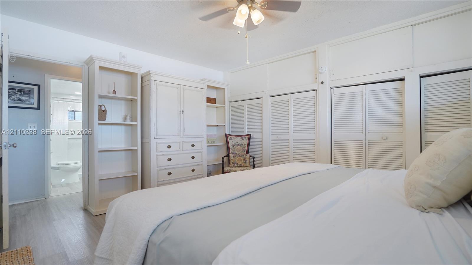 Built-in floor-to-ceiling storage cabinetry with louvered doors, integrated shelving unit, wood-finish flooring, and a ceiling fan with integrated lighting