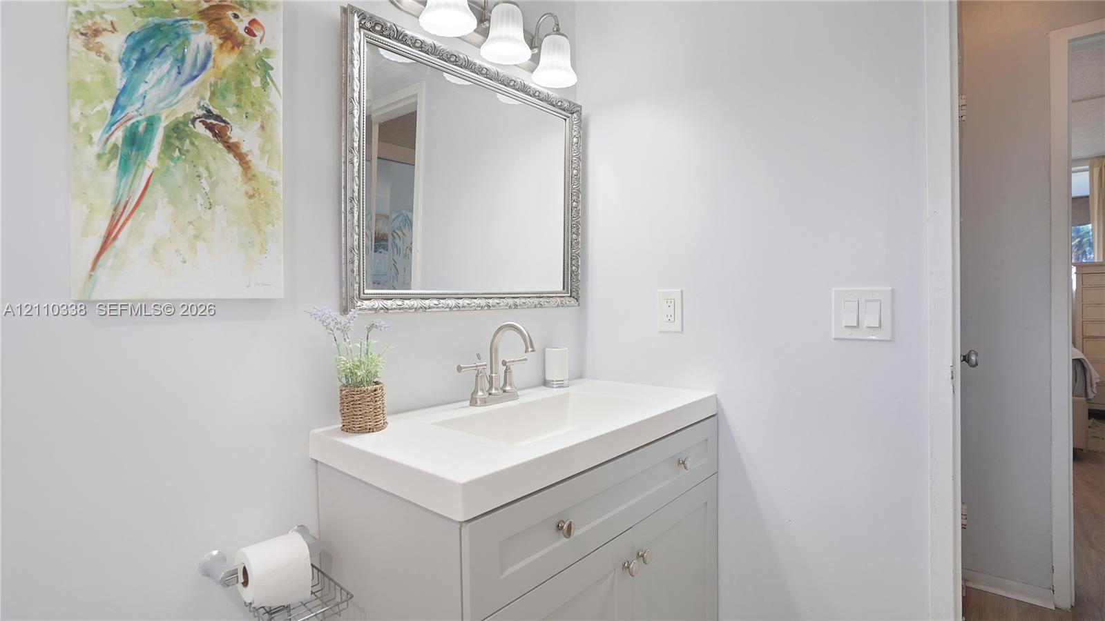 Gray vanity with integrated rectangular sink and polished nickel faucet, topped by a framed rectangular wall mirror and a three-light vanity fixture