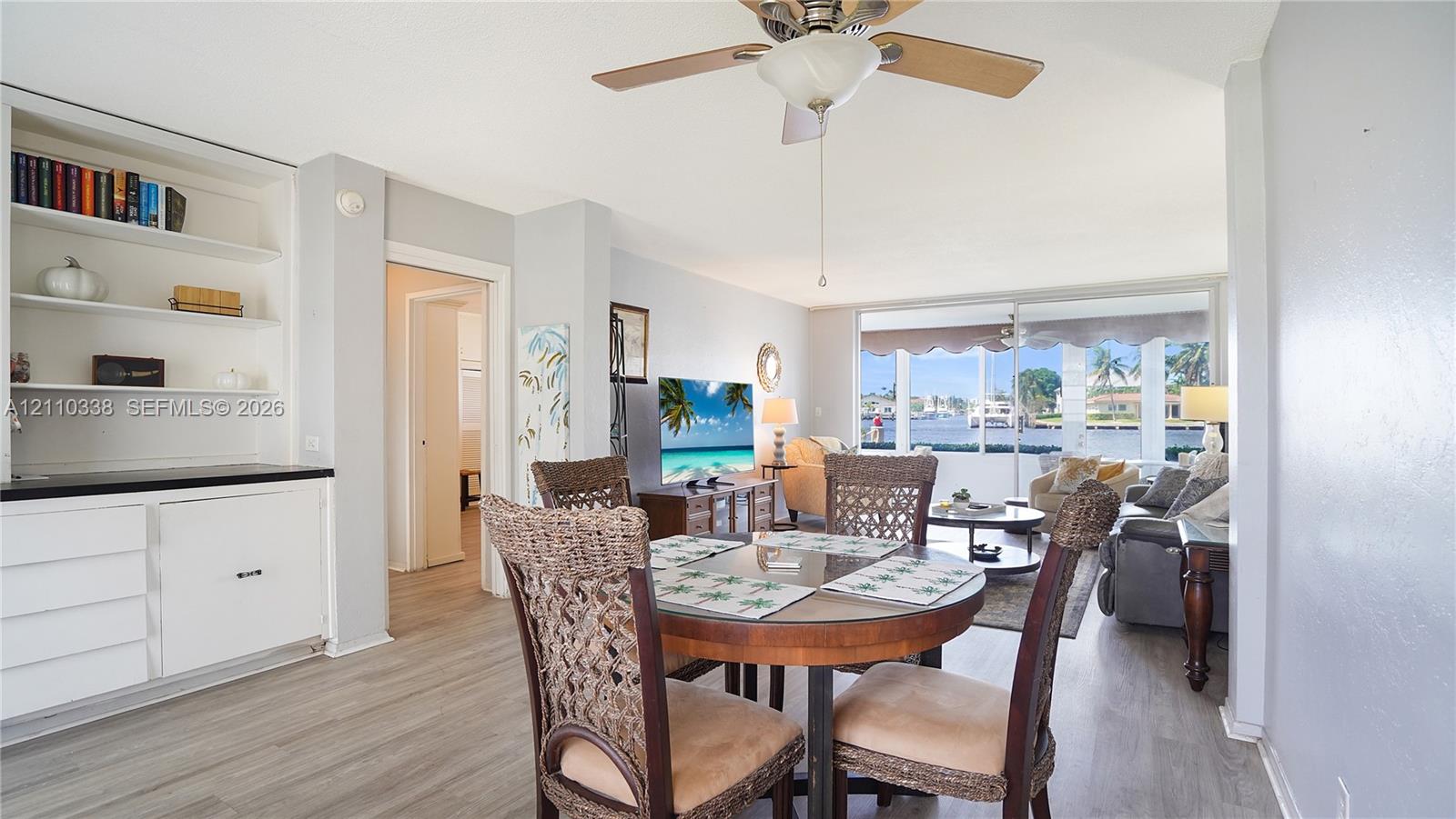 Living area featuring wood-finish flooring, floor-to-ceiling glass sliding doors, built-in shelving, white cabinetry with a stone-top surface, and a central ceiling fan