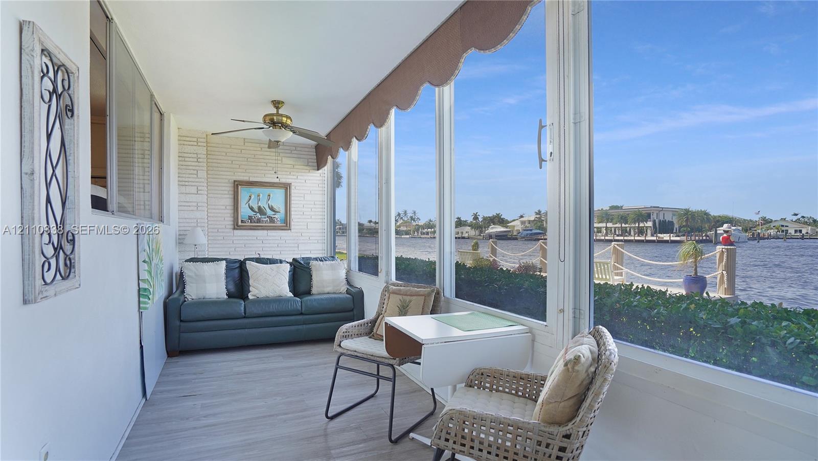 Enclosed porch featuring expansive floor-to-ceiling windows, white painted brick masonry, wood-finish flooring, a ceiling-mounted fan, and direct water exposure