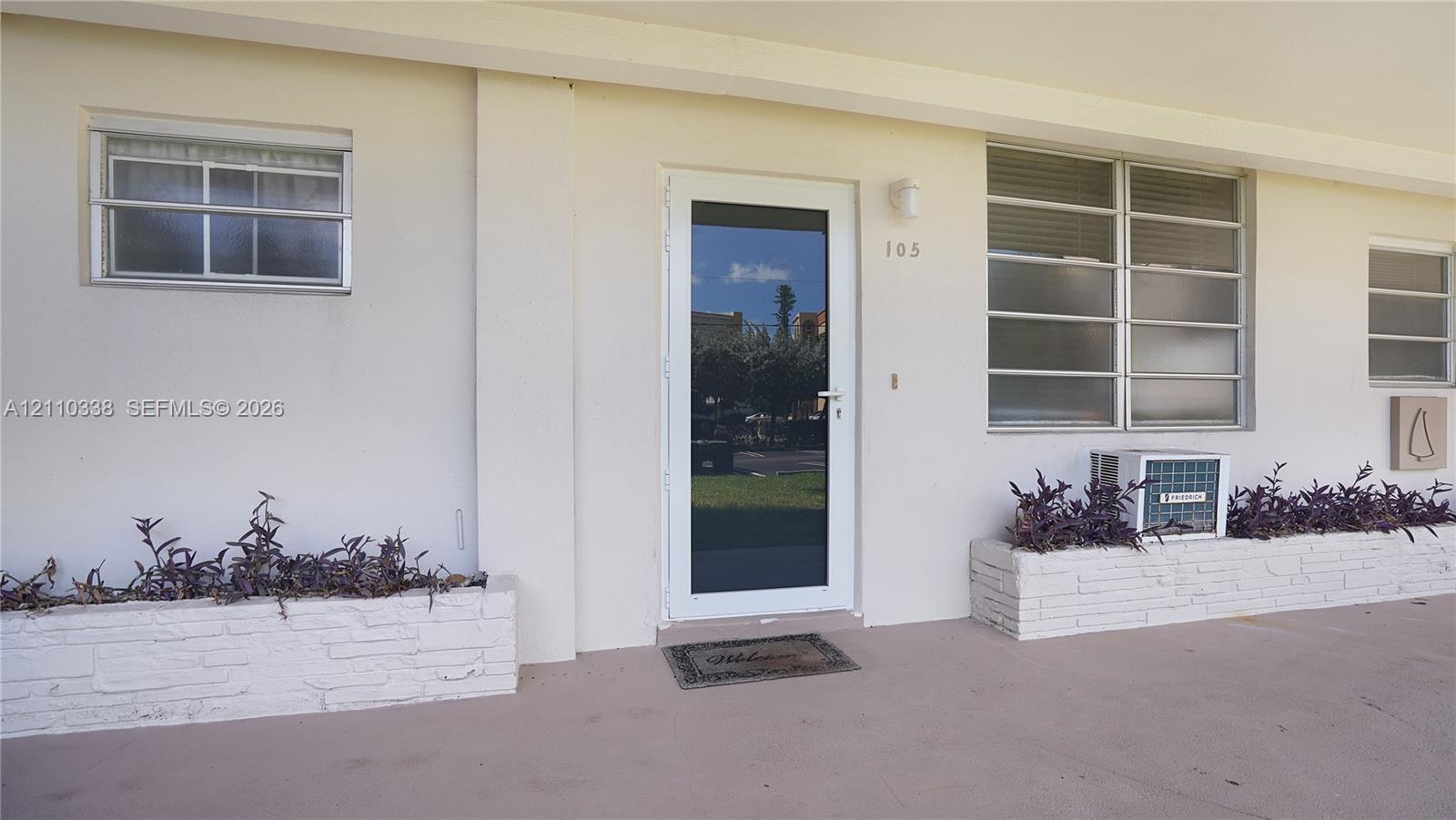 Exterior entrance featuring a white-framed glass door, horizontal-pane windows, and integrated brick-faced planters