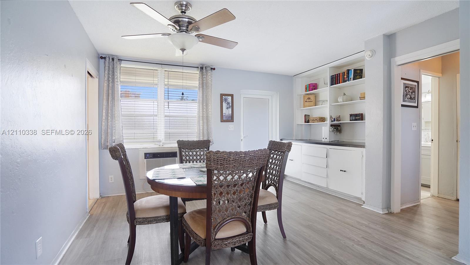 Dining area featuring wood-finish flooring, built-in white cabinetry with open shelving, and a central ceiling fan