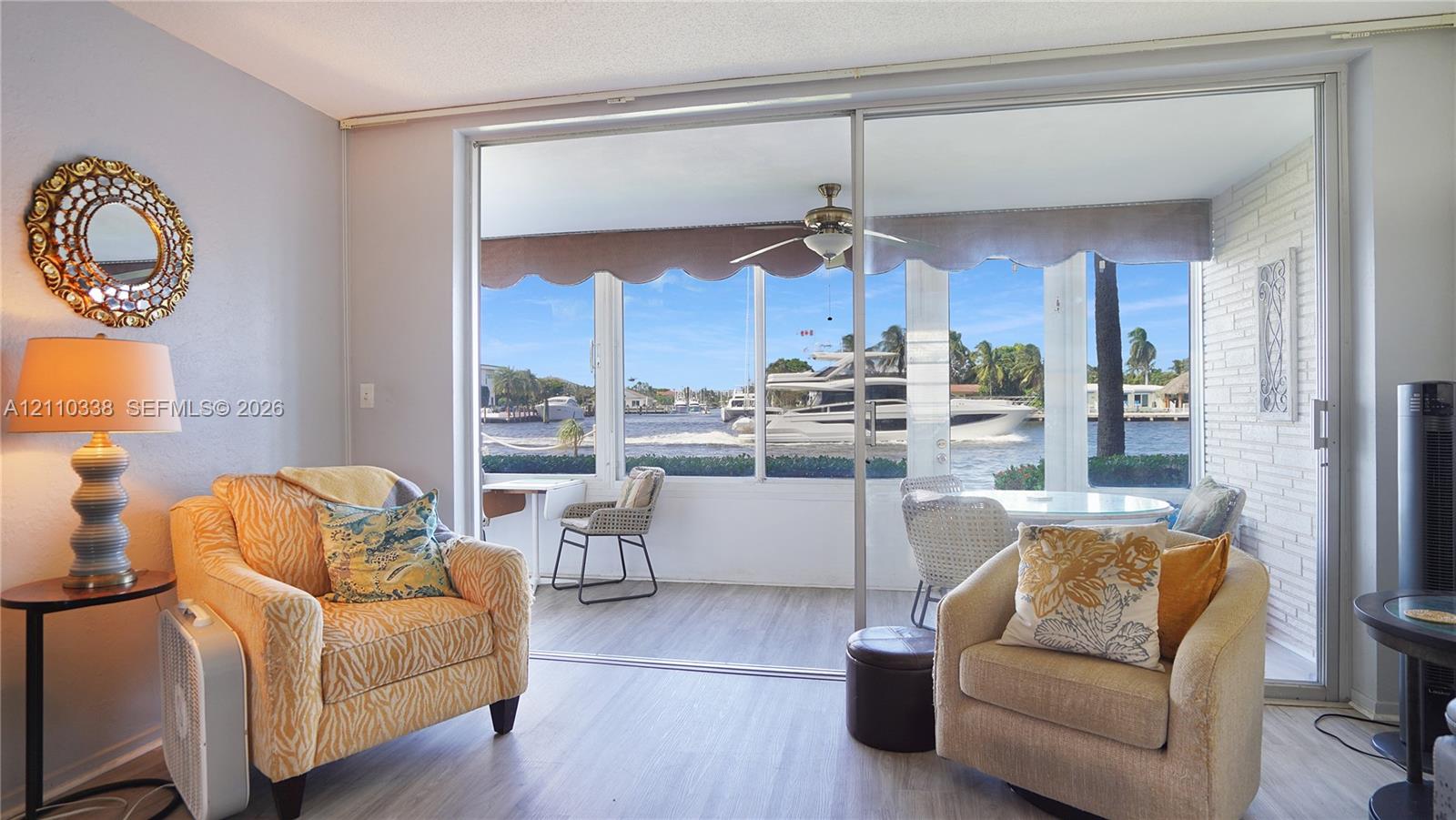 Large sliding glass doors opening to an enclosed patio with painted brick wall, wood-finish flooring, and waterfront scenery