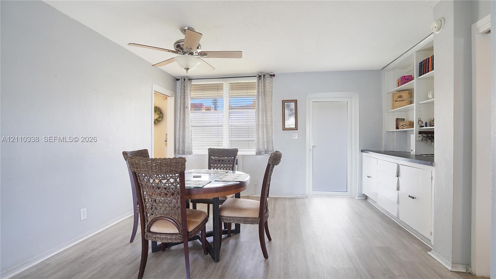 Interior space featuring light-toned wood-finish flooring, built-in floor-to-ceiling cabinetry with shelving, a ceiling fan with integrated lighting, and multi-pane windows