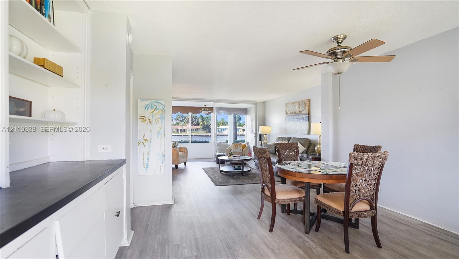 Open-concept floor plan featuring wood-finish flooring, built-in cabinetry with a dark countertop, a ceiling fan, and floor-to-ceiling windows