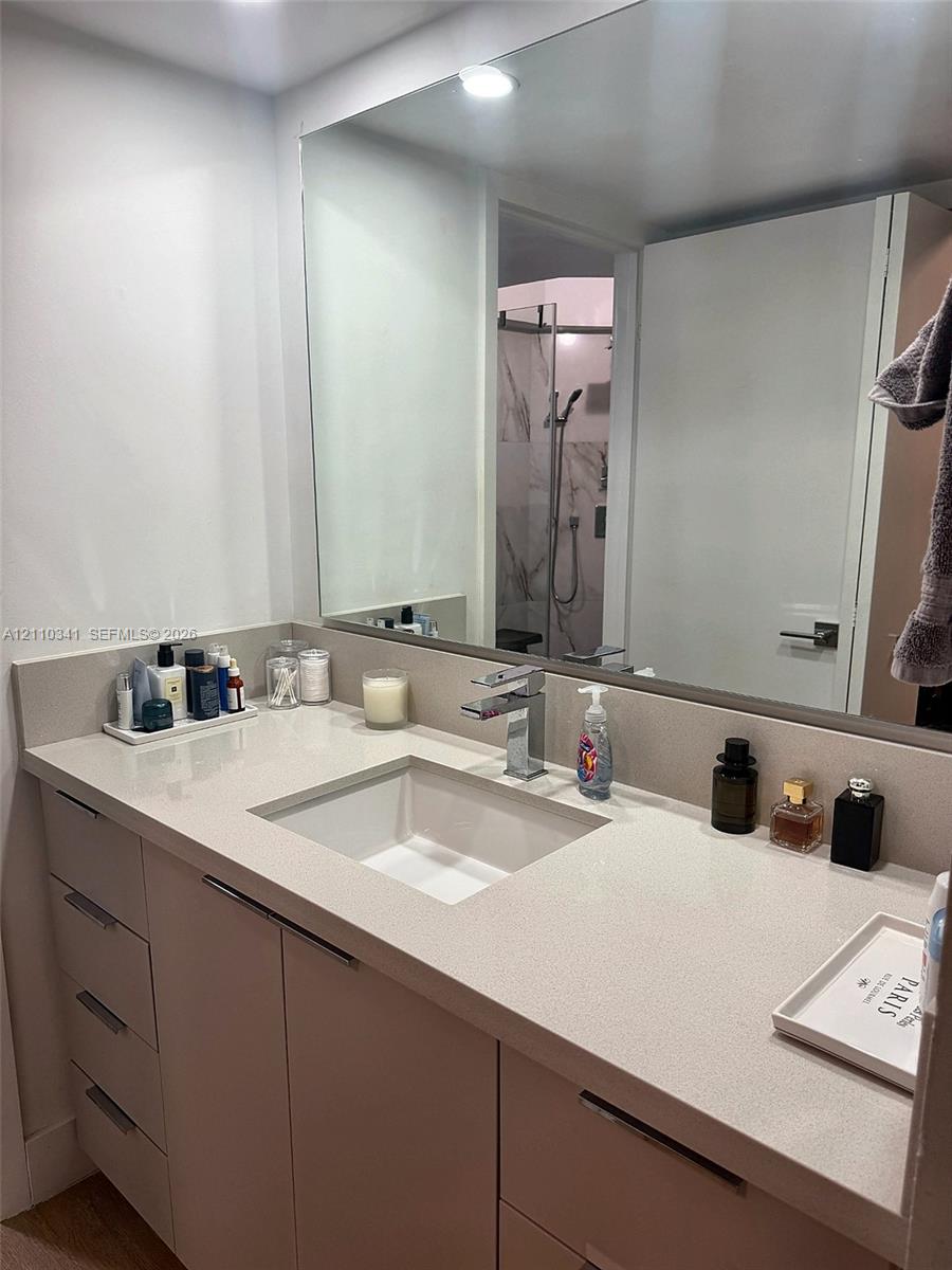 Custom vanity featuring stone-composite countertop, undermount rectangular sink, chrome single-handle faucet, integrated cabinet hardware, and expansive wall-mounted mirror Custom vanity featuring stone-composite countertop, undermount rectangular sink, chrome single-handle faucet, integrated cabinet hardware, and expansive wall-mounted mirror