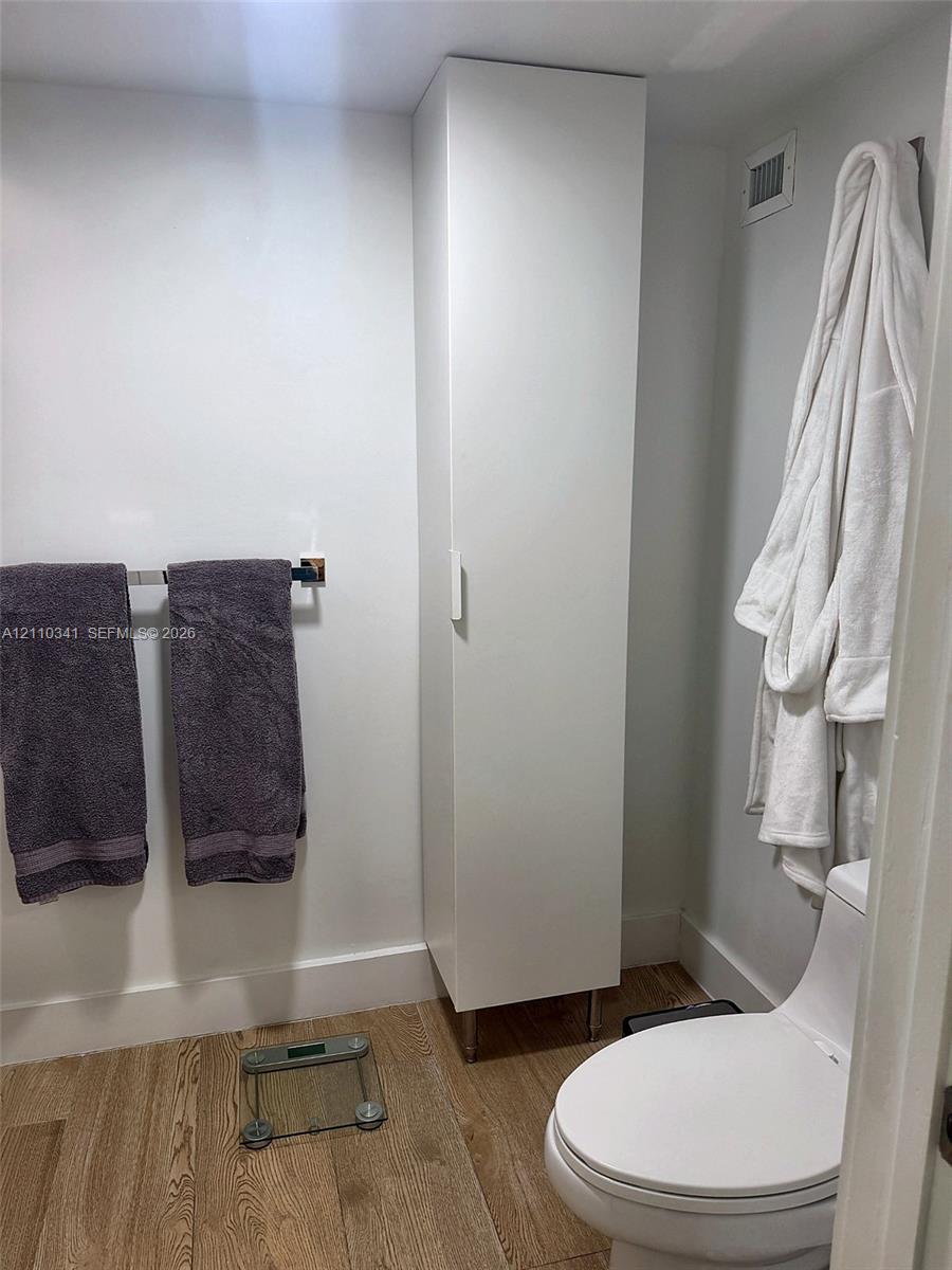 Full-height white storage cabinetry, wood-finish flooring, and a contemporary white toilet Full-height white storage cabinetry, wood-finish flooring, and a contemporary white toilet