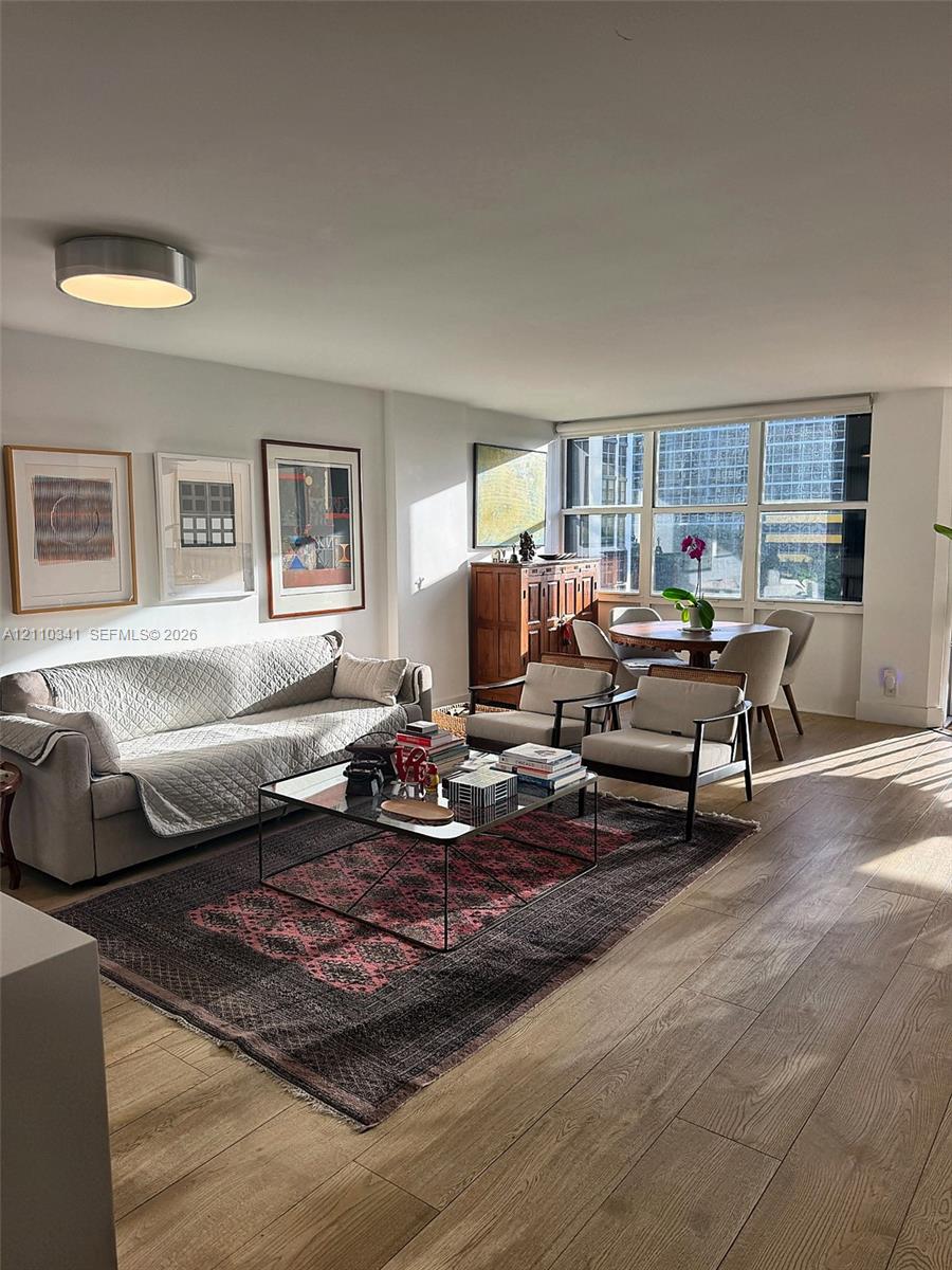 Living area featuring wood-finish flooring, floor-to-ceiling windows, and a flush-mount ceiling light Living area featuring wood-finish flooring, floor-to-ceiling windows, and a flush-mount ceiling light